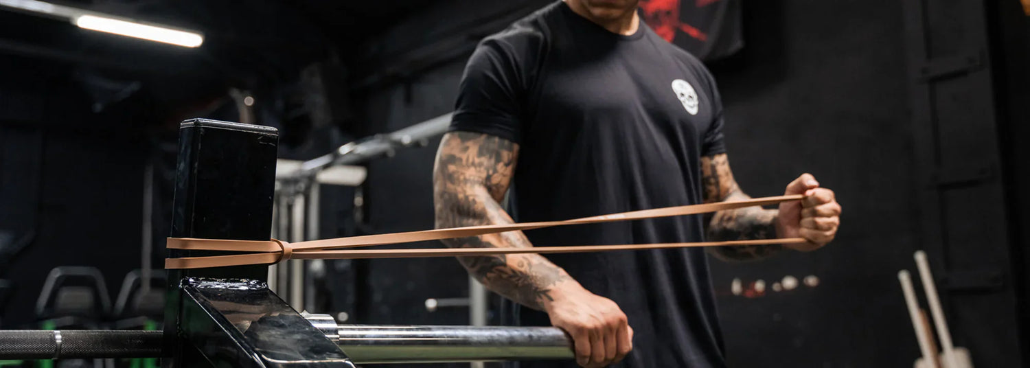 An athlete in a black tee shirt performs a banded pull apart using a tan resistance band.