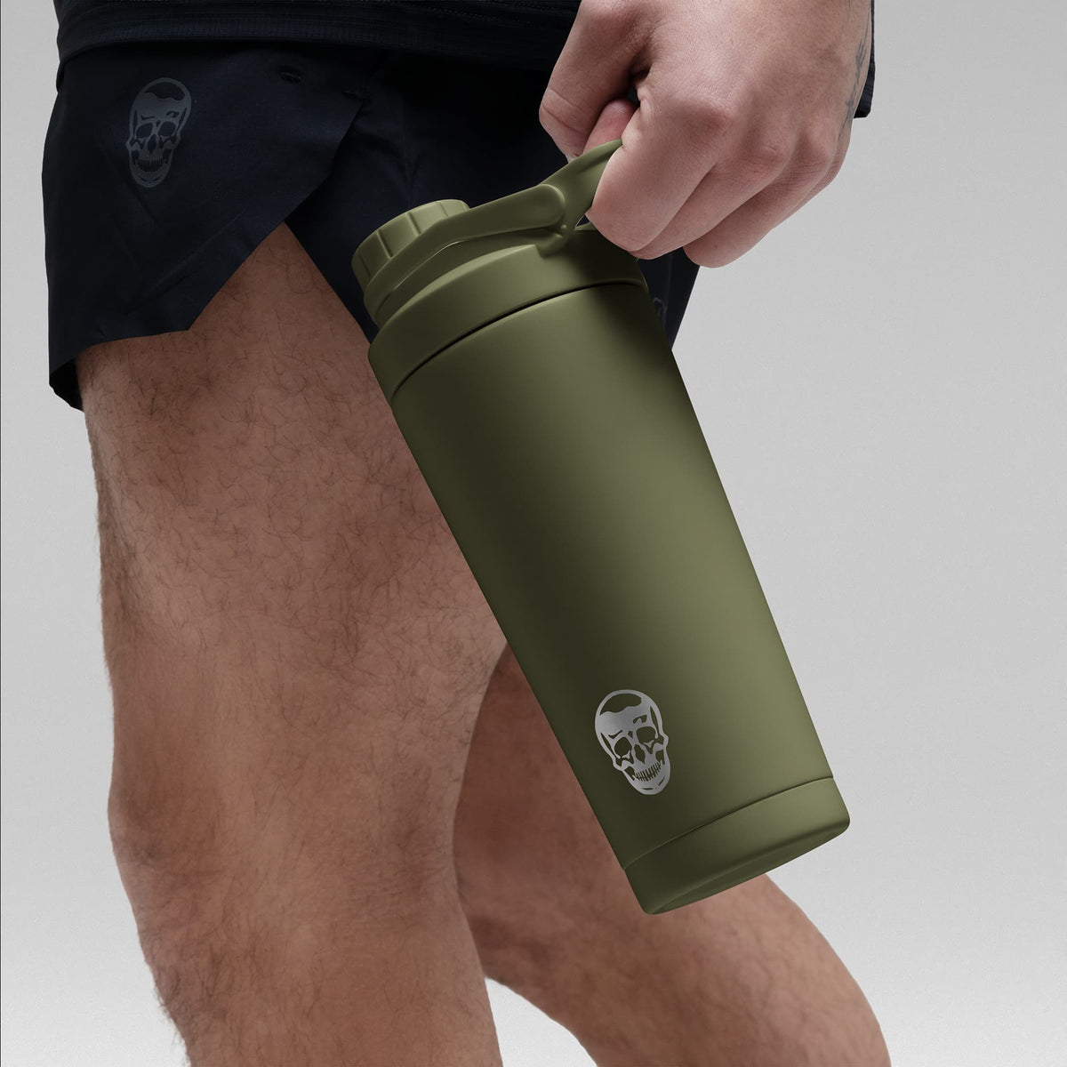 Athlete holding the OD Green stainless steel shaker bottle by the built in carry loop handle with the skull logo facing outward