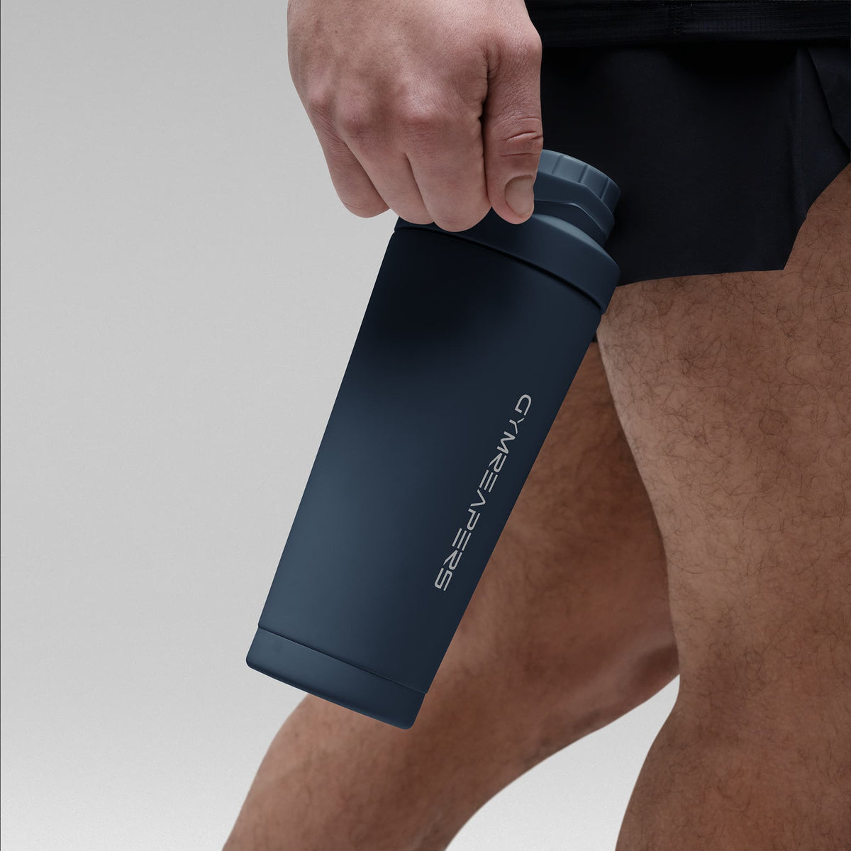 Athlete holding the Navy blue stainless steel shaker bottle by the built in carry loop handle with the wordmark logo facing outward