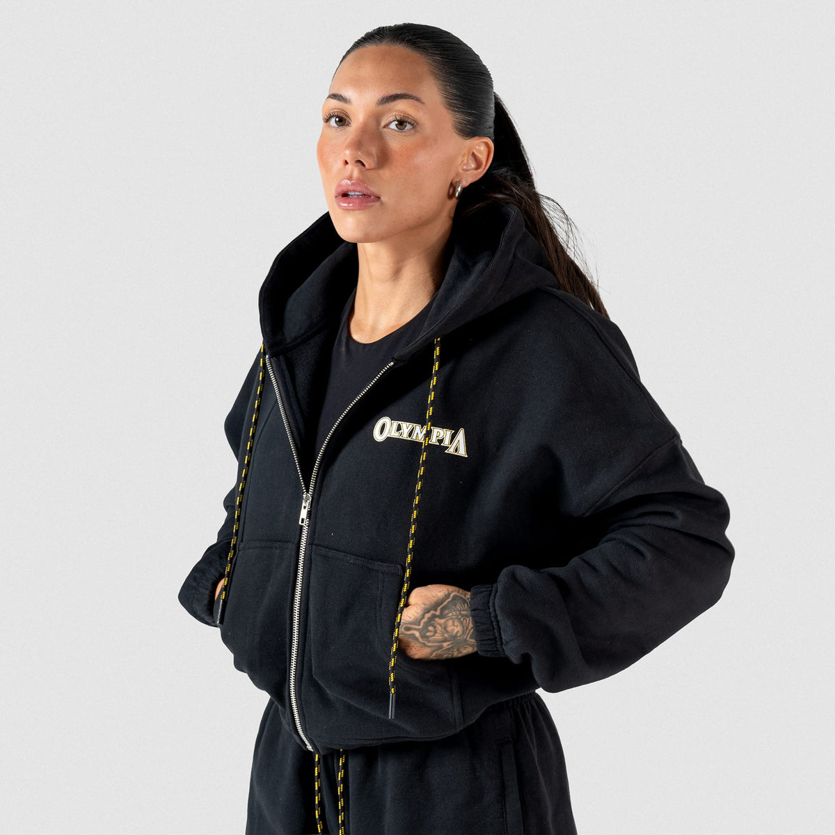 Champions Gold Cropped Zip-Up Hoodie |  Front View, on model of half zipped hoodie, gold and black adjustable drawstrings, and "Olympia" wordmark logo