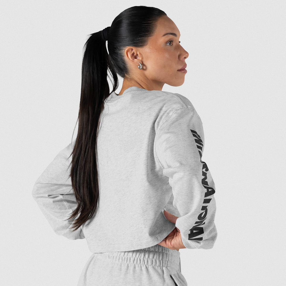 Back and slightly angled view of female model wearing the Olympia International Division Crop Long Sleeve in gray