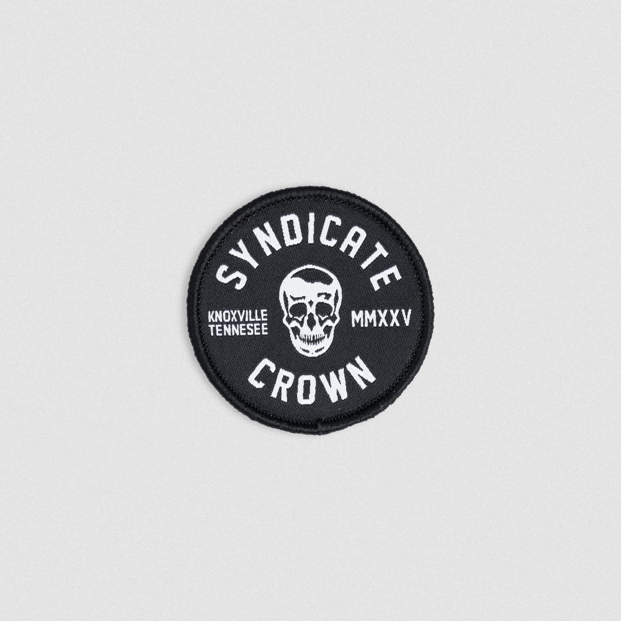 Black round SYNDICATE x MMXXV patch with white embroidered skull, Knoxville Tennessee text, and hook backing for gear or bag attachment.
