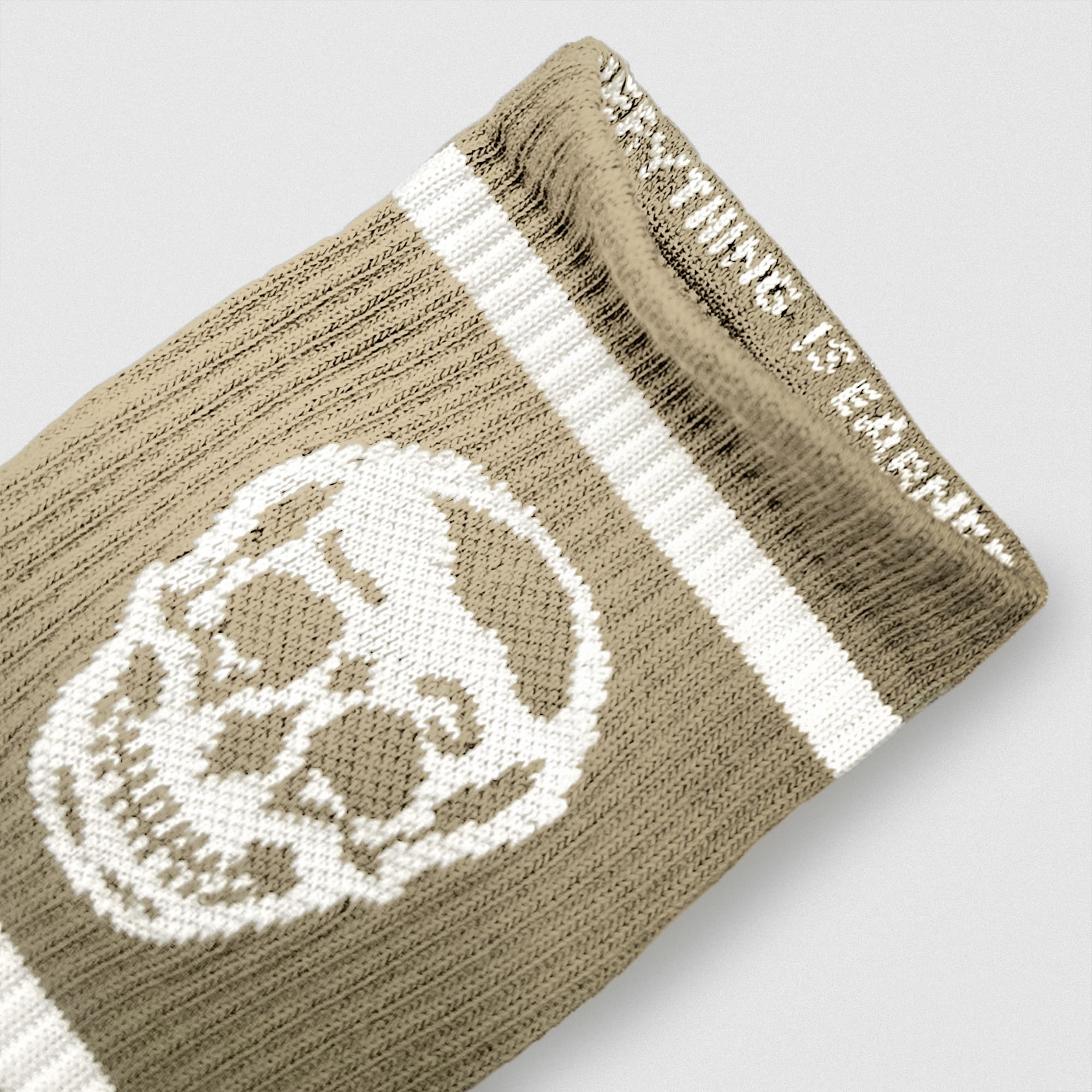 Close-up of a sand Gymreapers wristband featuring a white skull design and woven mantra along the inner cuff.